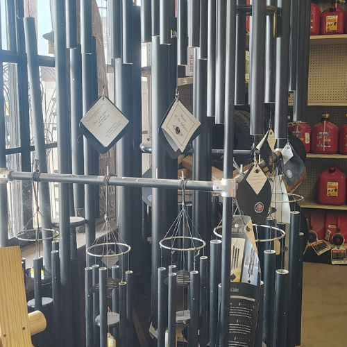 Display of assorted black and silver wind chimes hanging in a shop, with informational tags and red fire extinguishers on shelves behind.
