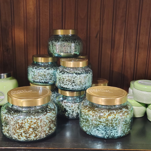 Decorative green-and-white speckled glass jars with gold lids are stacked on a dark shelf against warm wood paneling, creating a cozy vintage display.