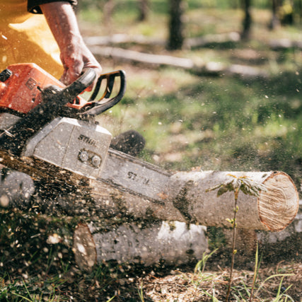 STIHL EquipmentA person uses a chainsaw to cut through a log in a forest, scattering wood chips. The scene conveys ruggedness and focus in a natural setting.
