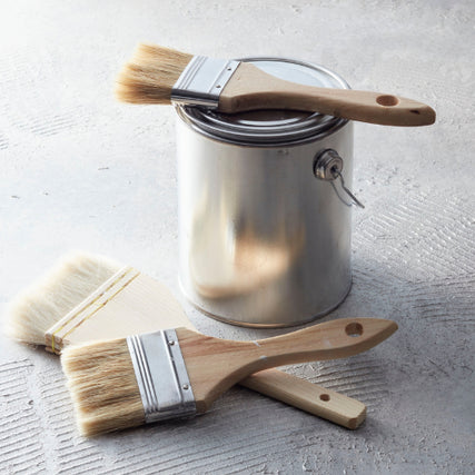 Paint & SuppliesA closed metallic paint can on a textured surface, with two natural-bristle paintbrushes placed beside and on top, evoking a sense of readiness for painting.